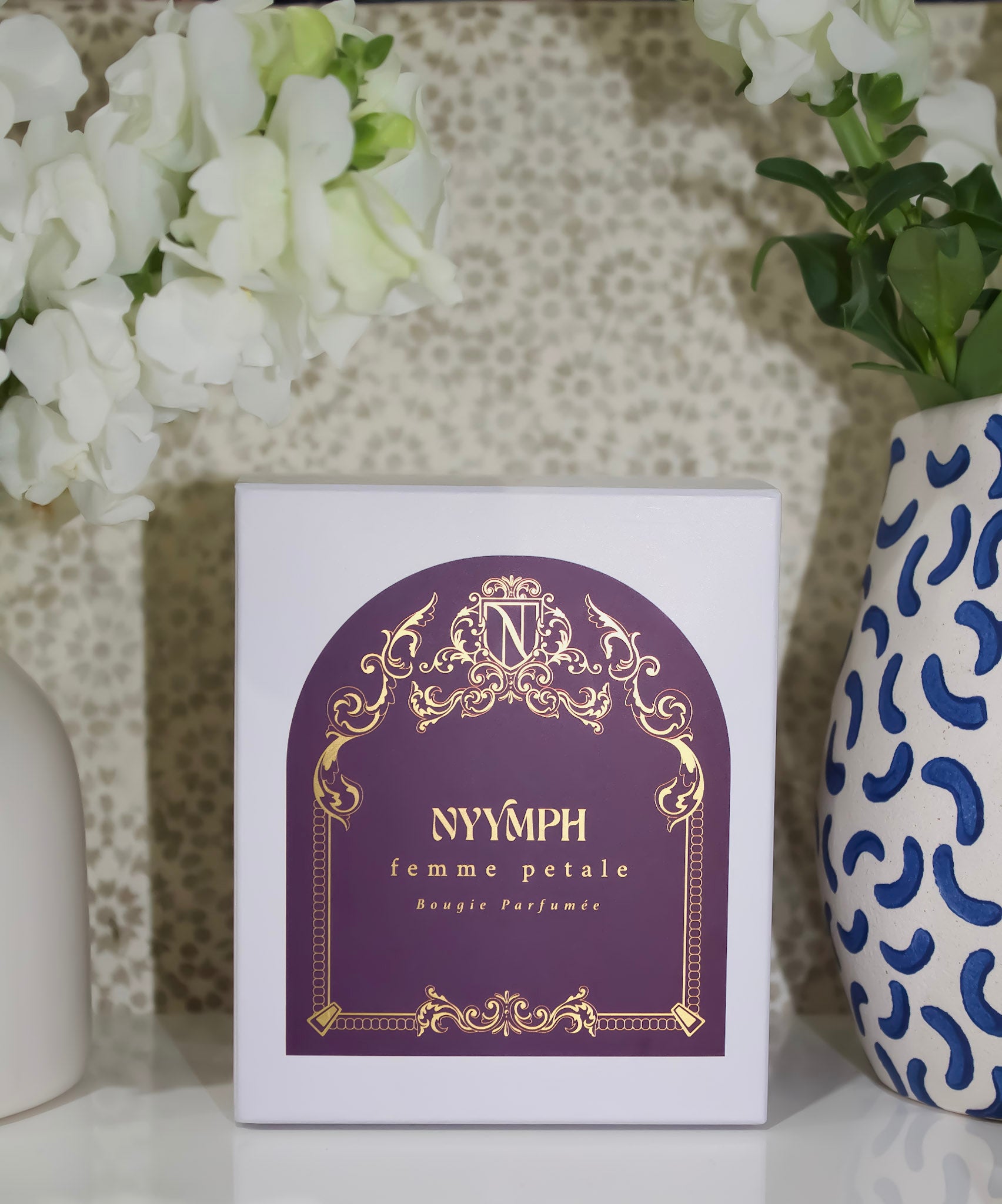 NYYMPH Femme Petale luxury candle box in gray with ornate gold and purple design, isolated on transparent background.